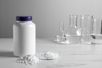 Photo of Calcium carbonate powder, jar and laboratory glassware on white marble table. Space for text