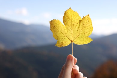 Photo of Woman holding beautiful autumn leaf in mountains, closeup. Space for text