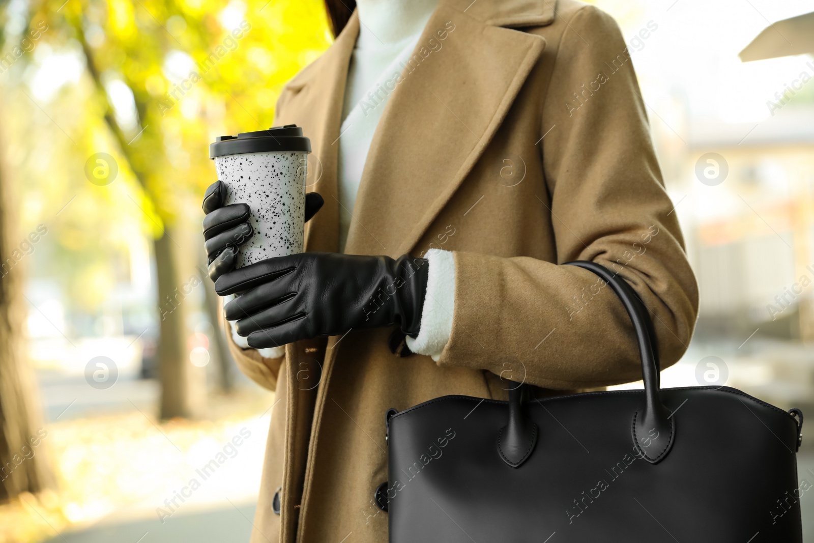 Photo of Woman with stylish leather gloves and cup of coffee on city street, closeup