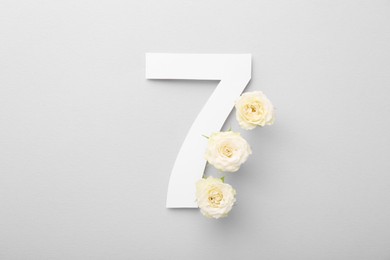 Paper number 7 and beautiful rose flowers on light grey background, top view