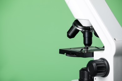 Photo of Modern medical microscope with glass slide on green background, closeup. Space for text