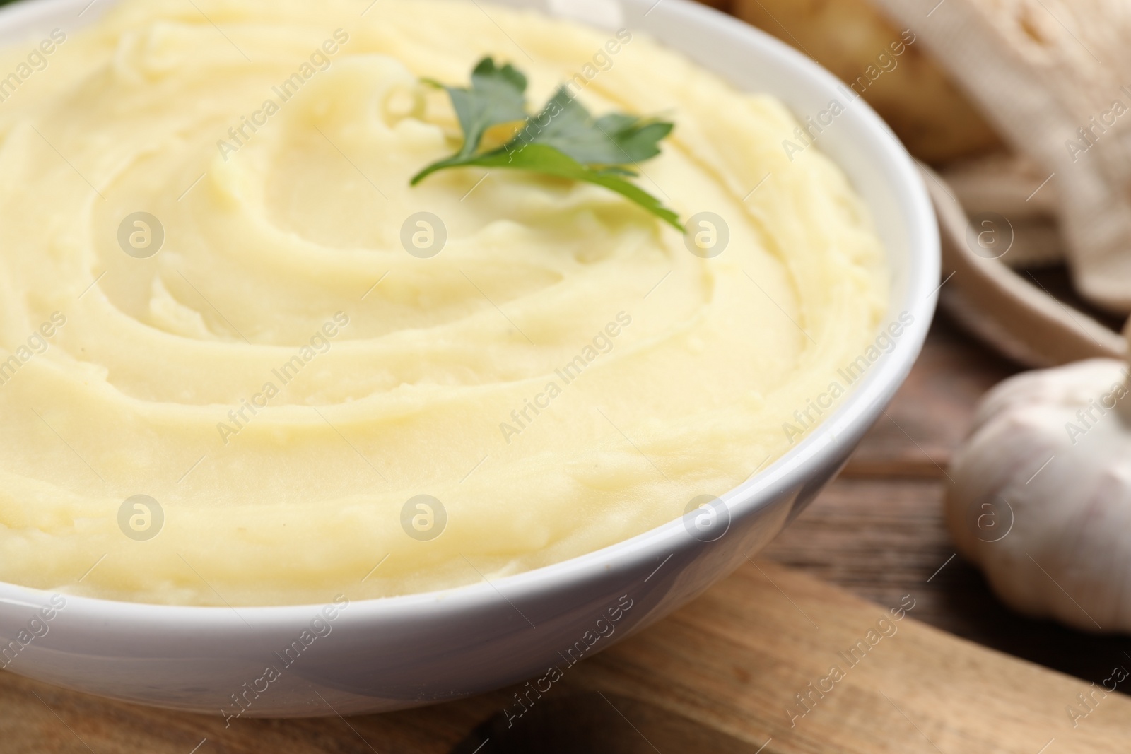 Photo of Bowl of tasty mashed potato, parsley and garlic on wooden table, closeup