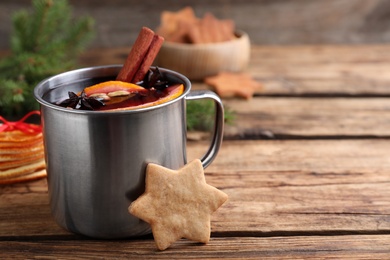 Photo of Aromatic mulled wine and cookie on wooden table, closeup. Space for text