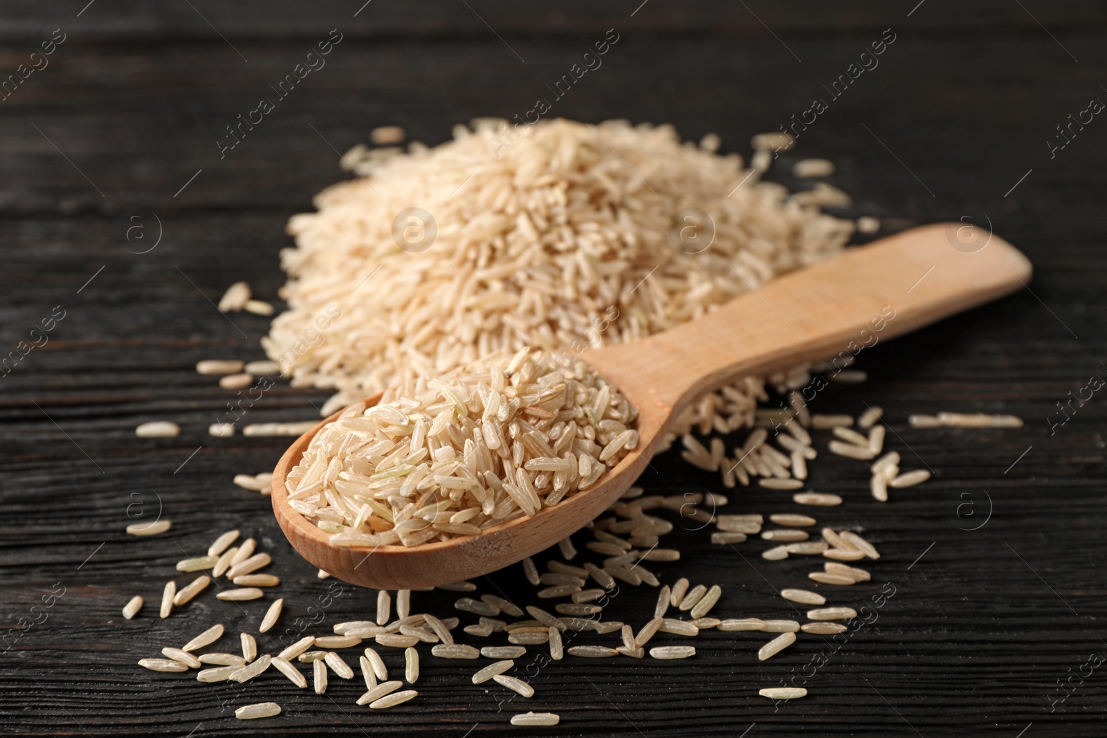 Photo of Uncooked brown rice in wooden spoon on table