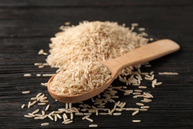 Photo of Uncooked brown rice in wooden spoon on table