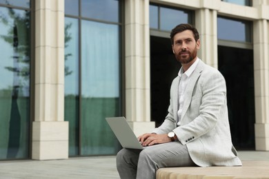 Handsome businessman with laptop on city street