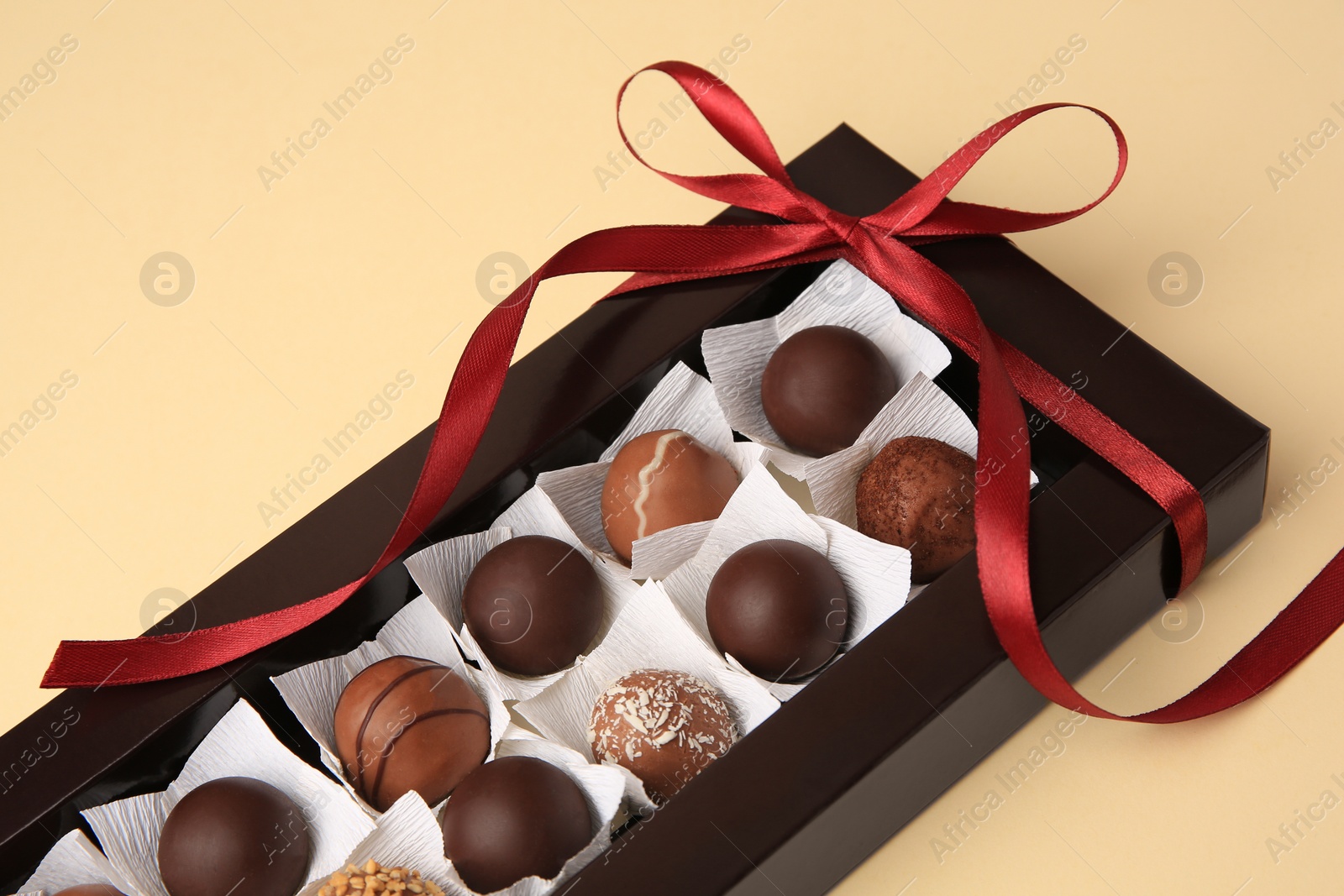 Photo of Box with delicious chocolate candies on beige table, closeup