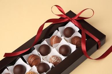 Box with delicious chocolate candies on beige table, closeup