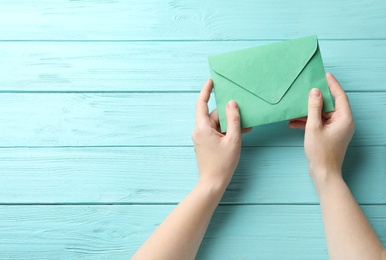 Photo of Woman with green paper envelope at light blue wooden table, top view. Space for text