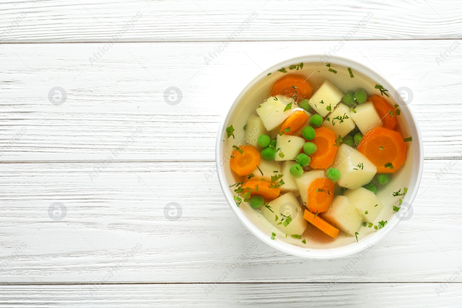 Photo of Bowl of fresh homemade vegetable soup on white wooden background, top view. Space for text