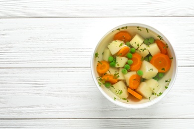 Bowl of fresh homemade vegetable soup on white wooden background, top view. Space for text