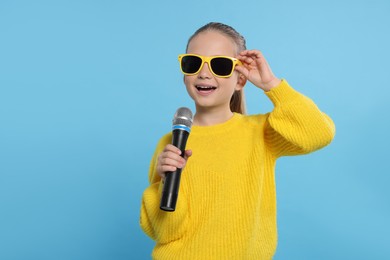 Photo of Cute little girl with microphone singing on light blue background