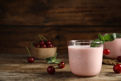 Photo of Tasty fresh milk shake with cherries on wooden table. Space for text