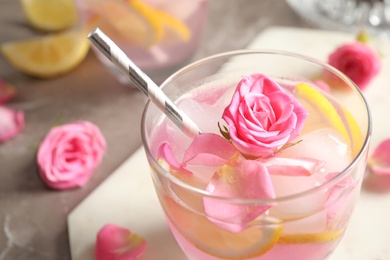 Photo of Glass of delicious refreshing drink with lemon and roses on table, closeup