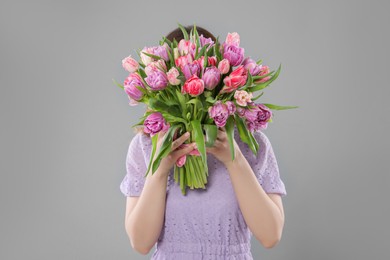 Photo of Woman covering her face with bouquet of beautiful tulips on grey background