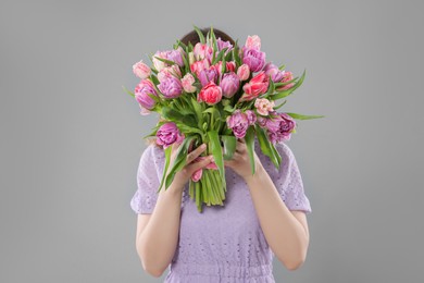 Woman covering her face with bouquet of beautiful tulips on grey background