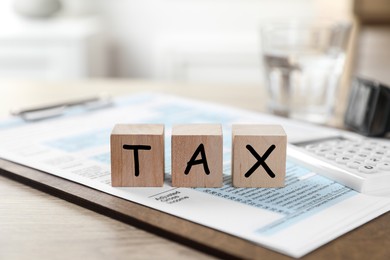 Wooden cubes with word Tax and document on table, closeup