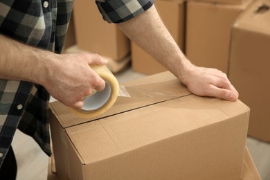 Photo of Man taping cardboard box indoors, closeup view