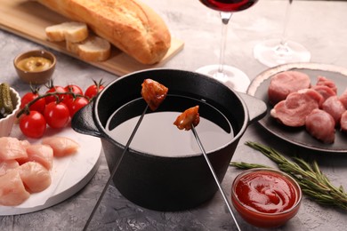 Photo of Fondue pot, forks with fried meat pieces and other products on grey textured table