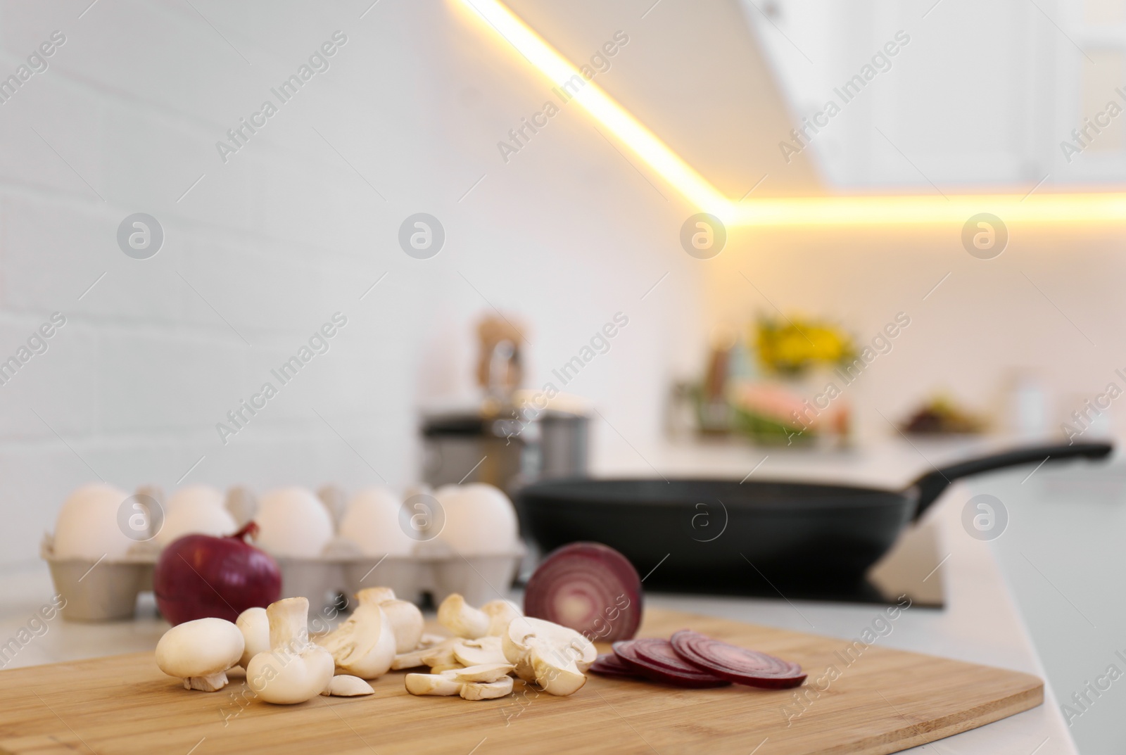 Photo of Wooden board with onion and mushrooms on kitchen counter