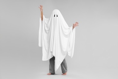 Photo of Woman in white ghost costume on light grey background. Halloween celebration
