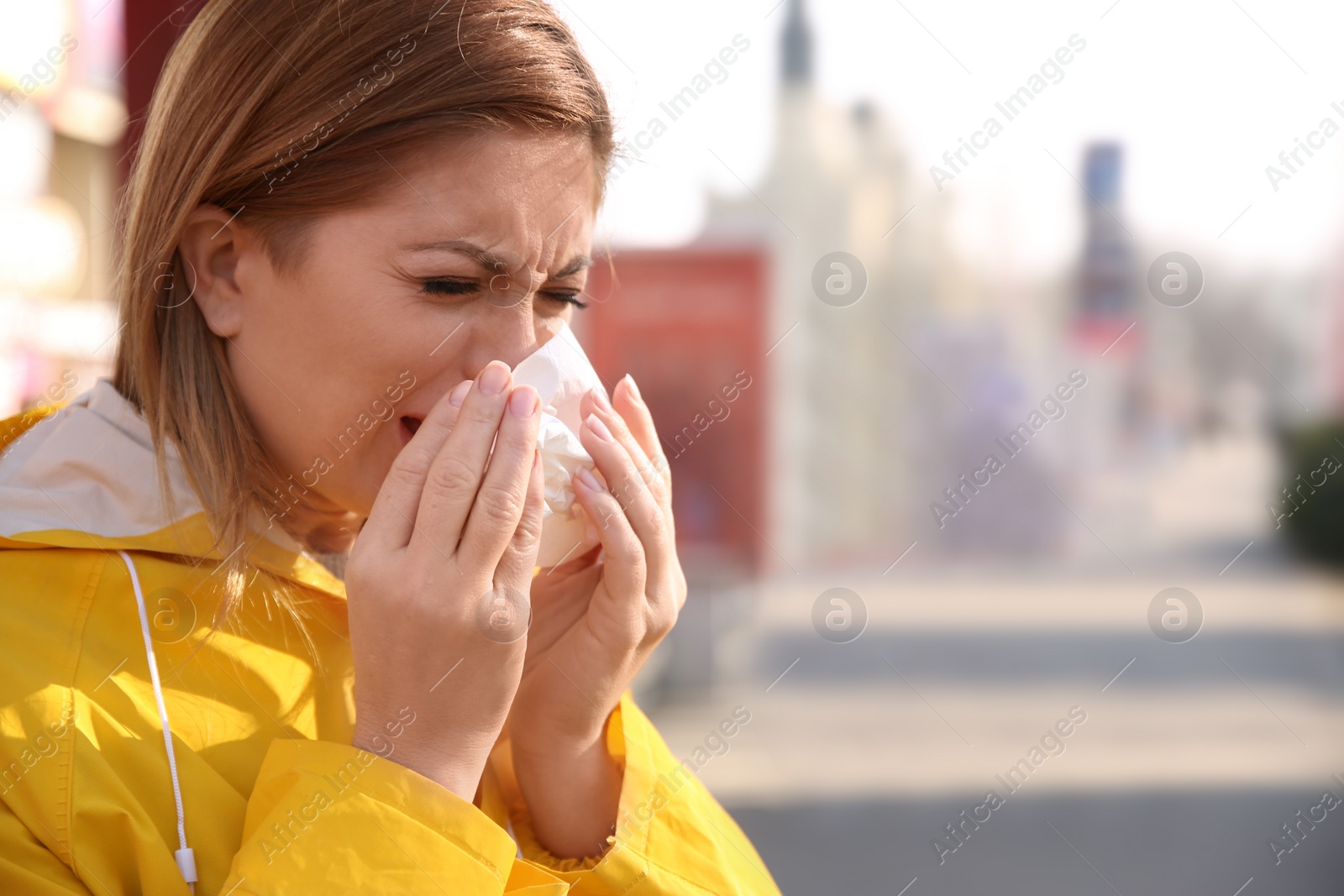 Photo of Sick woman sneezing on city street. Influenza virus