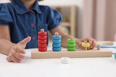 Photo of Motor skills development. Little girl playing with stacking and counting game at table indoors, closeup