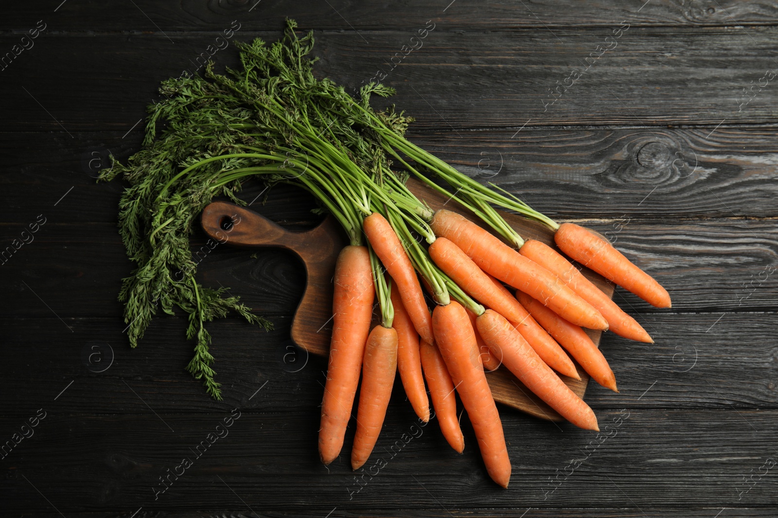 Photo of Board with ripe carrots on wooden background, top view