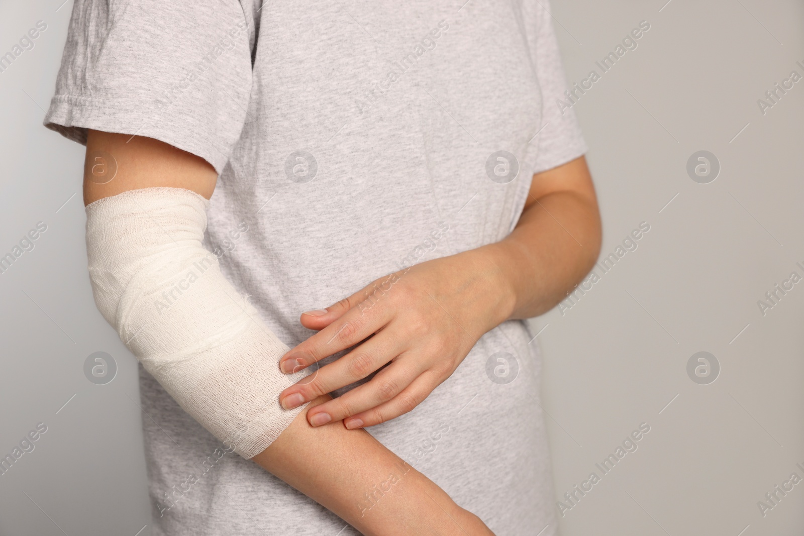 Photo of Woman with arm wrapped in medical bandage on light grey background, closeup