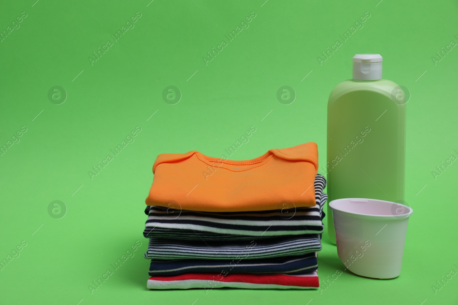 Photo of Stack of baby clothes and laundry detergents on light green background. Space for text