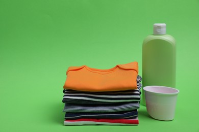 Photo of Stack of baby clothes and laundry detergents on light green background. Space for text