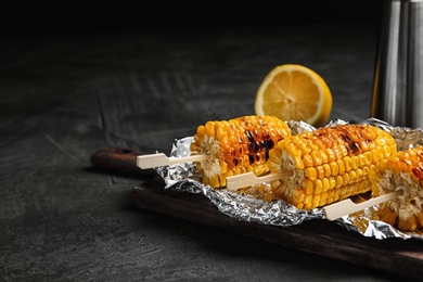 Photo of Foil with delicious grilled corn cobs on table