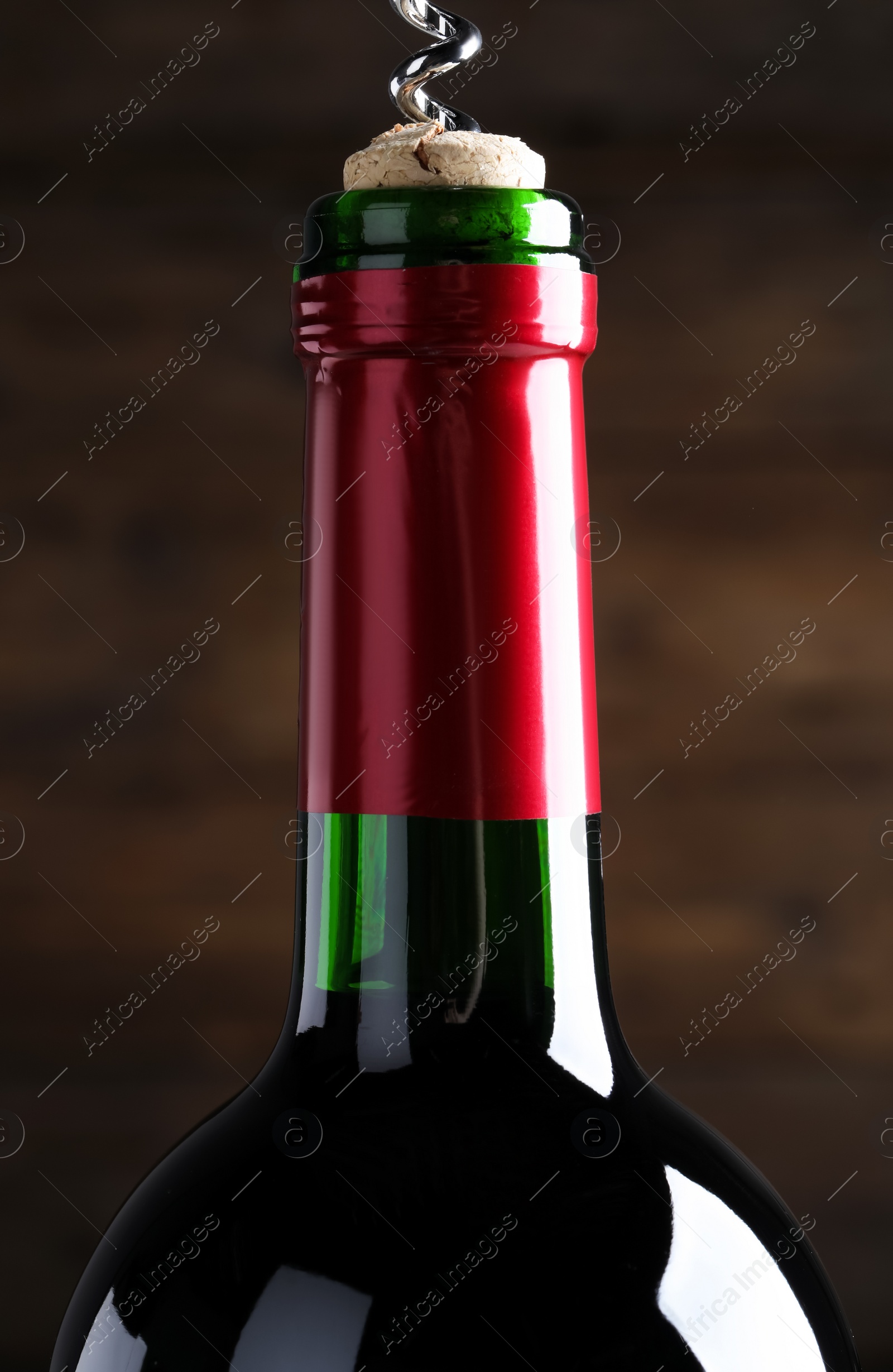 Photo of Opening wine bottle with corkscrew on dark brown background, closeup