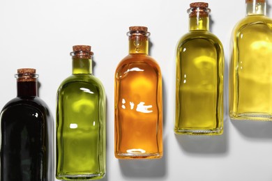 Photo of Vegetable fats. Different cooking oils in glass bottles on white background, flat lay