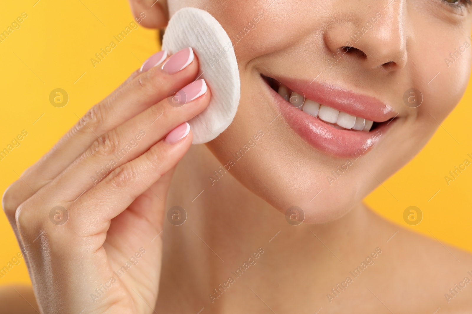 Photo of Beautiful woman removing makeup with cotton pad on orange background, closeup