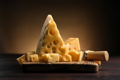 Photo of Pieces of delicious cheese and knife on wooden table
