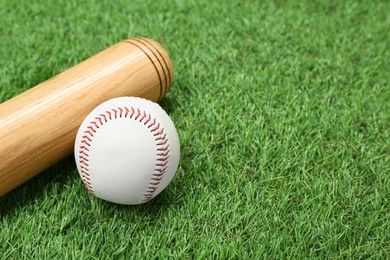 Photo of Wooden baseball bat and ball on green grass, closeup. Space for text