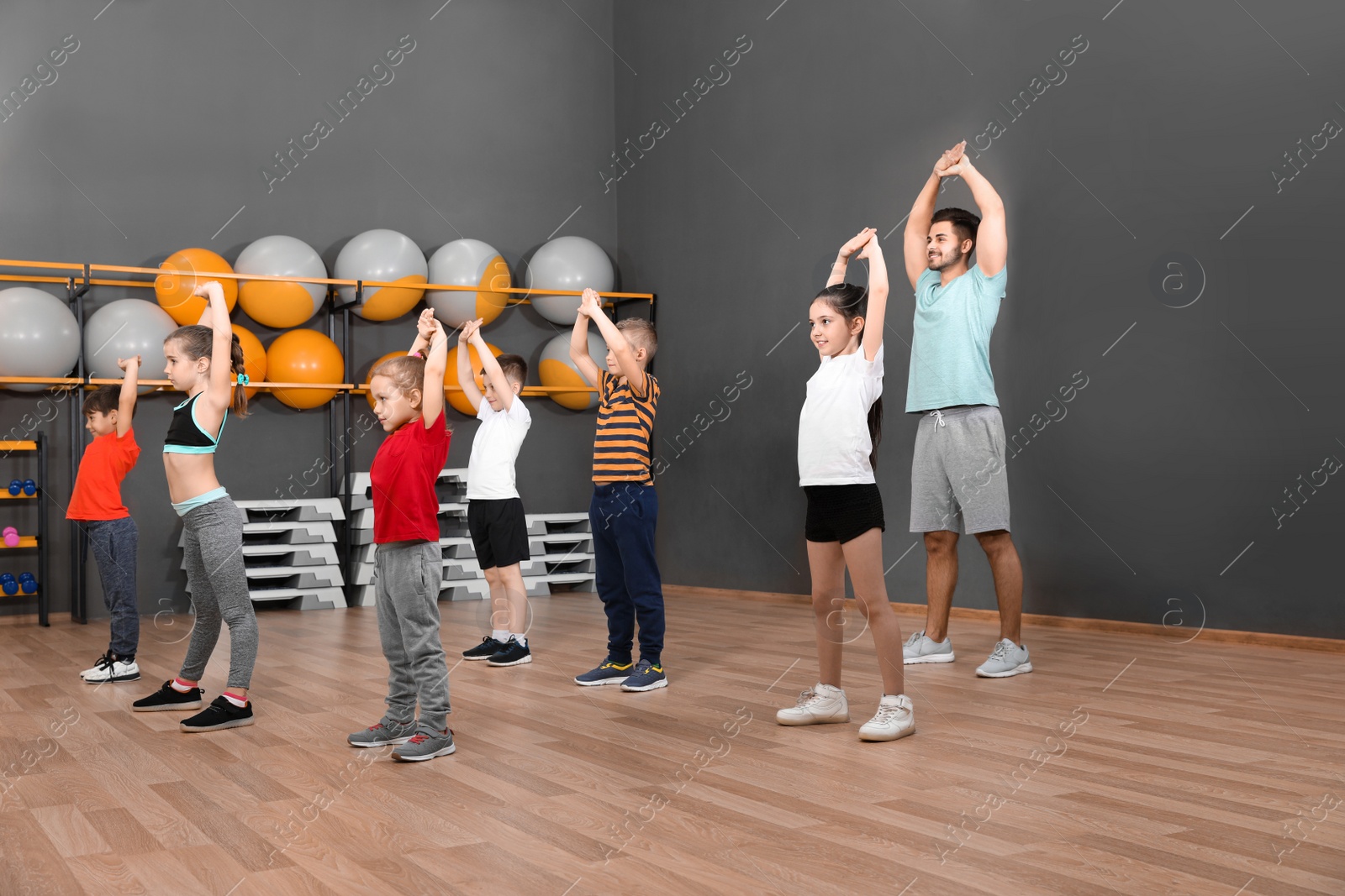 Photo of Cute little children and trainer doing physical exercise in school gym. Healthy lifestyle