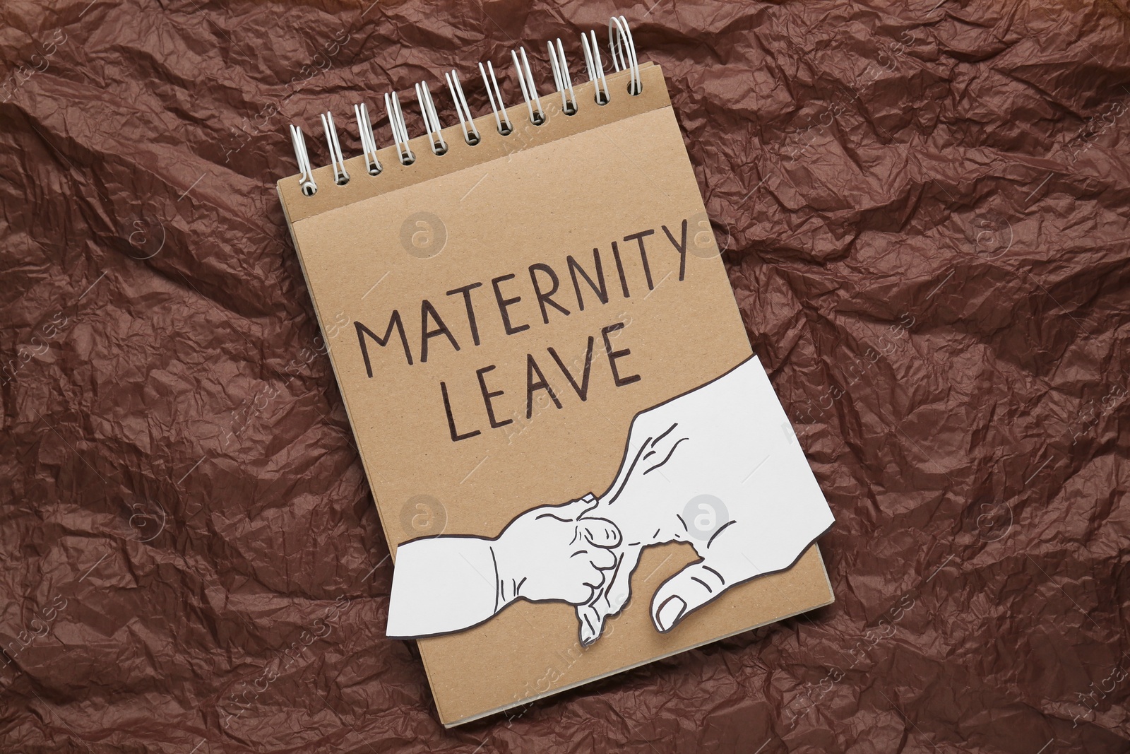Photo of Notepad with words Maternity Leave and cutout of hands on brown crumpled paper, top view