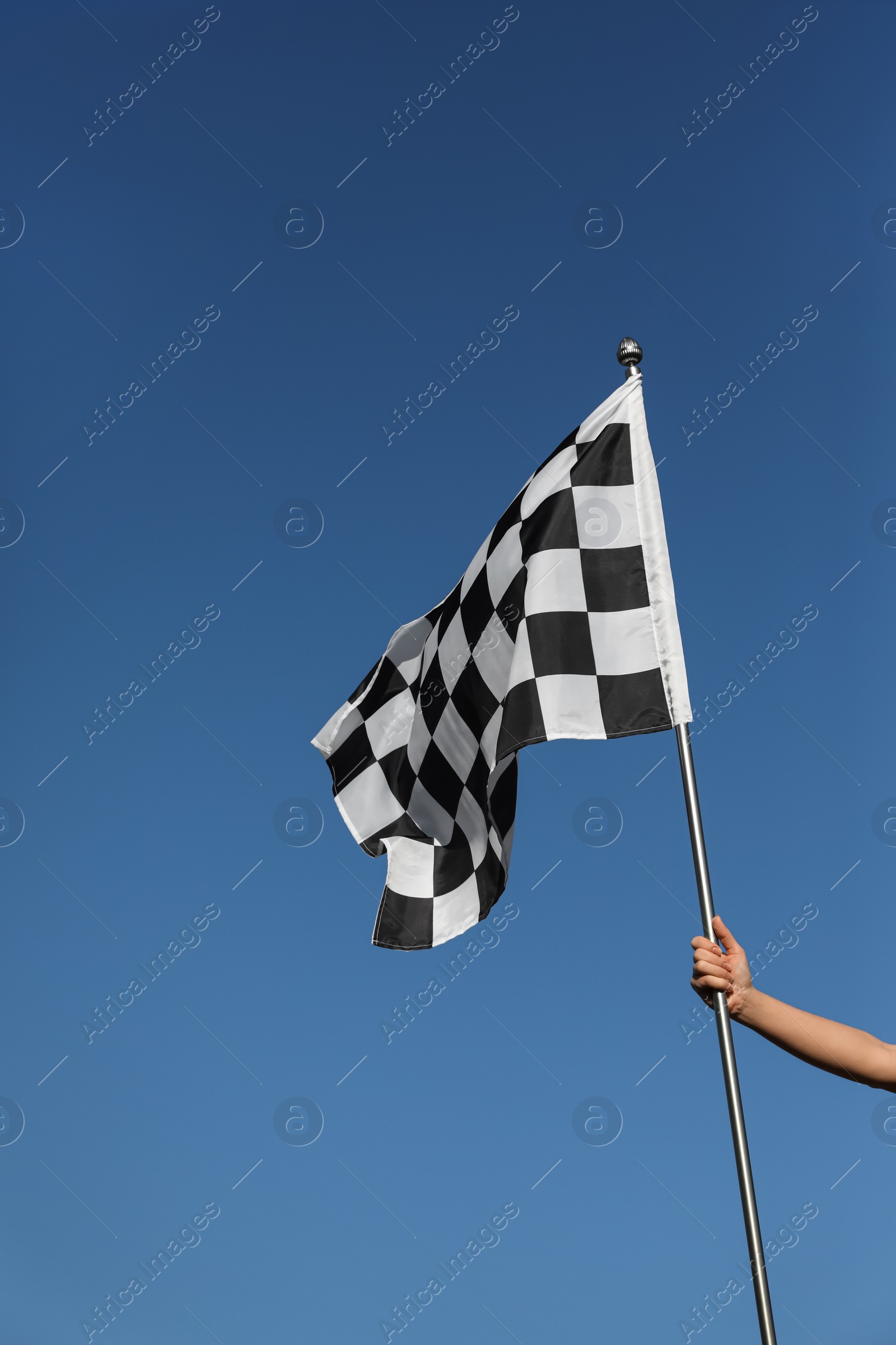 Photo of Woman holding checkered finish flag on light blue background, closeup
