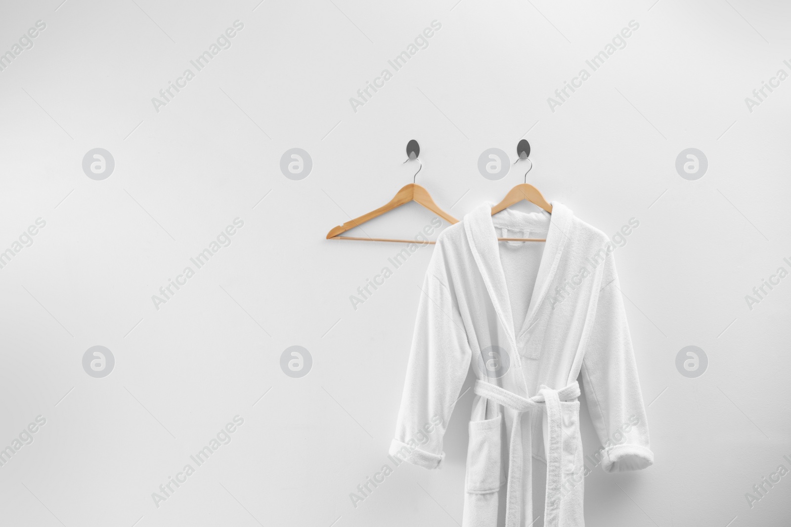 Photo of Soft comfortable bathrobe hanging on white wall, space for text