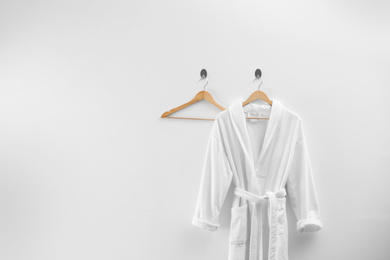 Soft comfortable bathrobe hanging on white wall, space for text