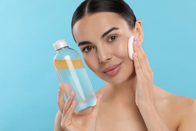 Photo of Beautiful woman removing makeup with cotton pad on light blue background, space for text