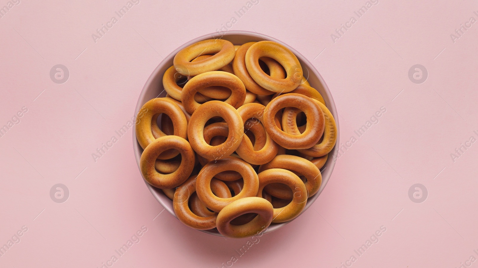Photo of Bowl of tasty dry bagels (sushki) on pink background, top view