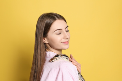 Young woman with boa constrictor on yellow background. Exotic pet