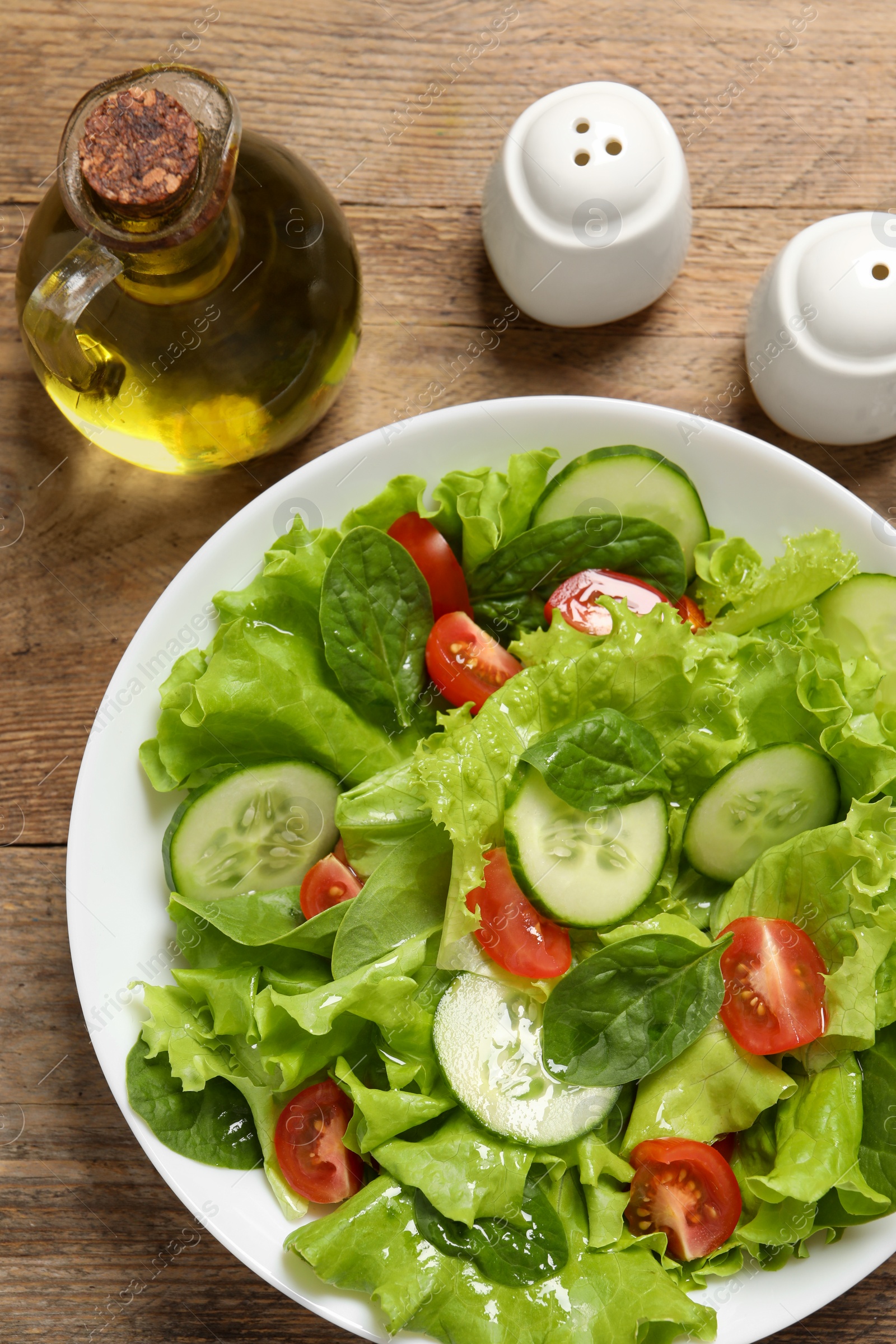 Photo of Delicious salad, oil, salt and pepper shakers on wooden table, flat lay