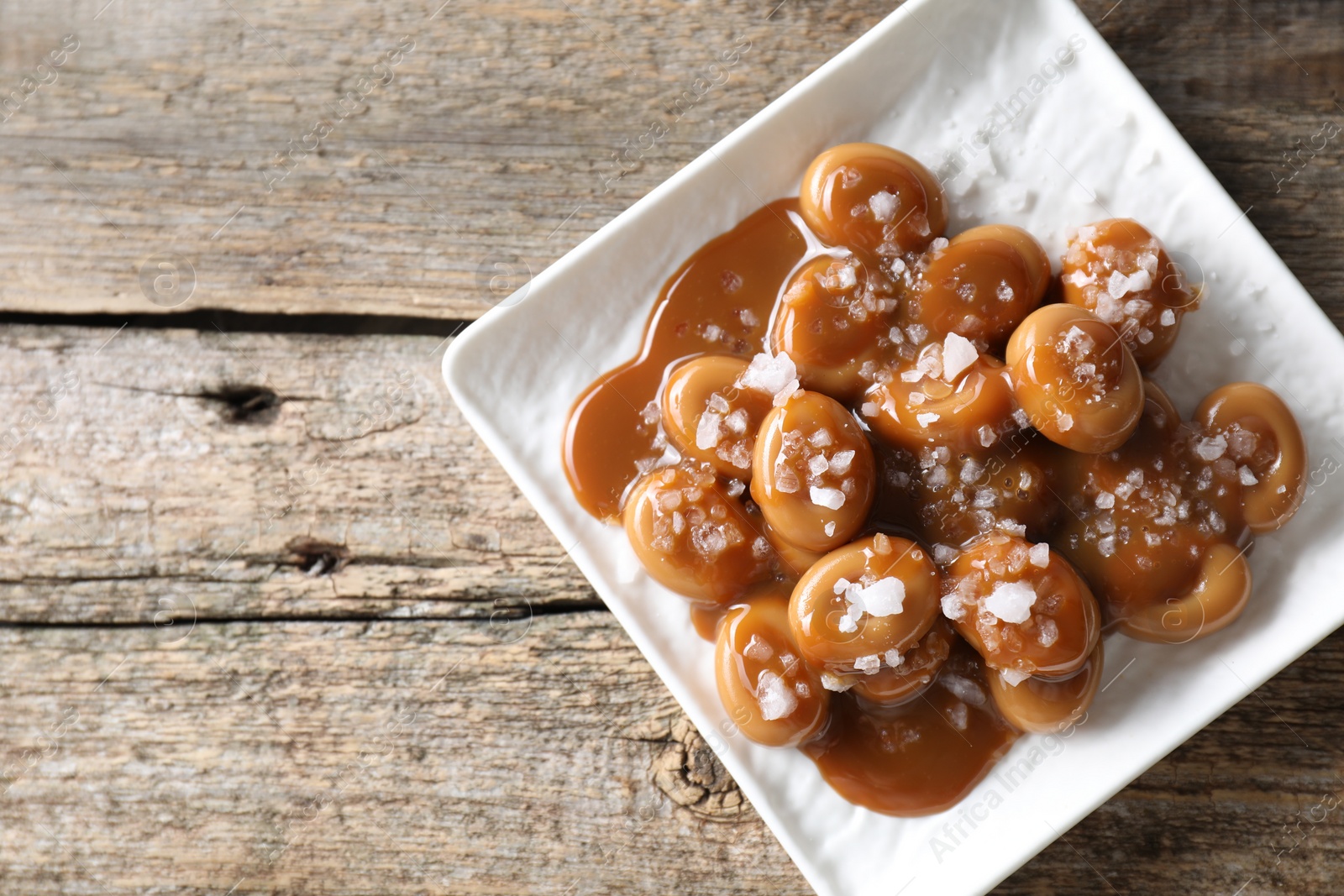 Photo of Tasty candies, caramel sauce and salt on wooden table, top view. Space for text