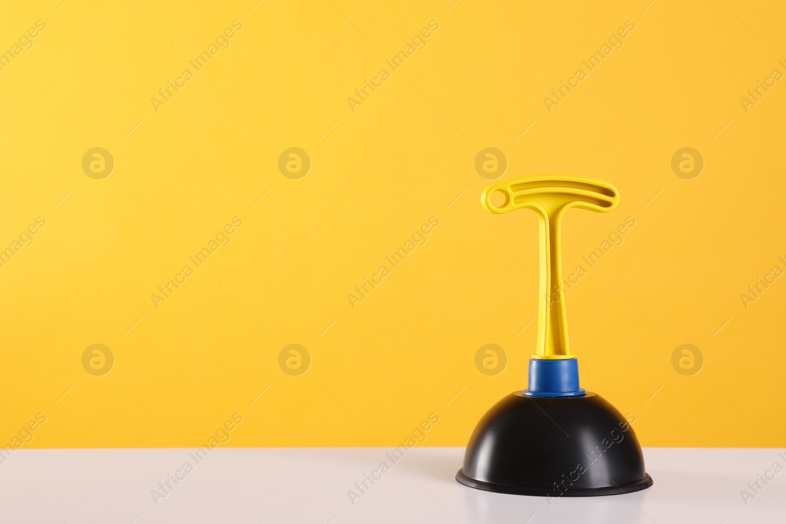 Photo of Plunger on white table against yellow background. Space for text