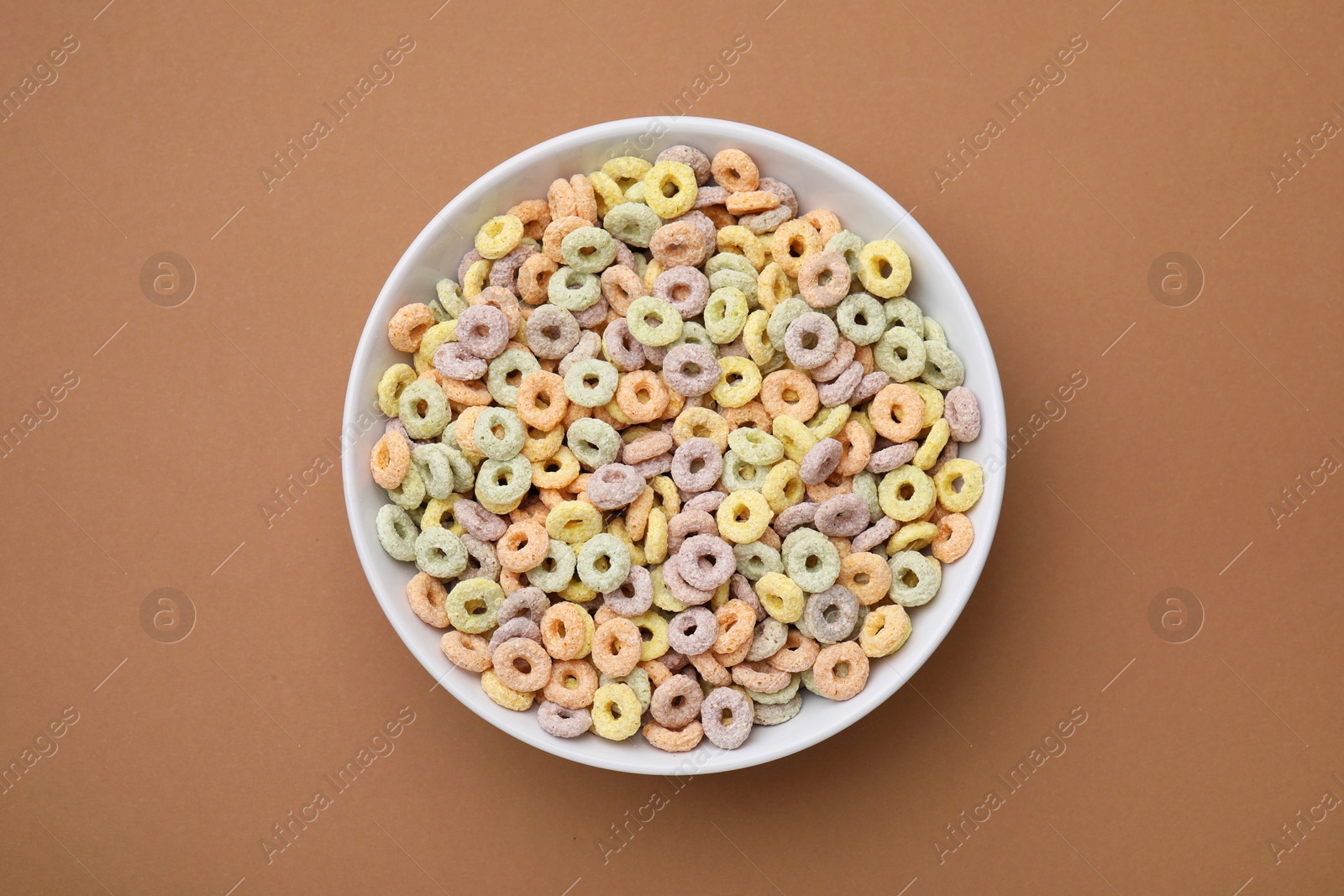 Photo of Tasty cereal rings in bowl on brown table, top view