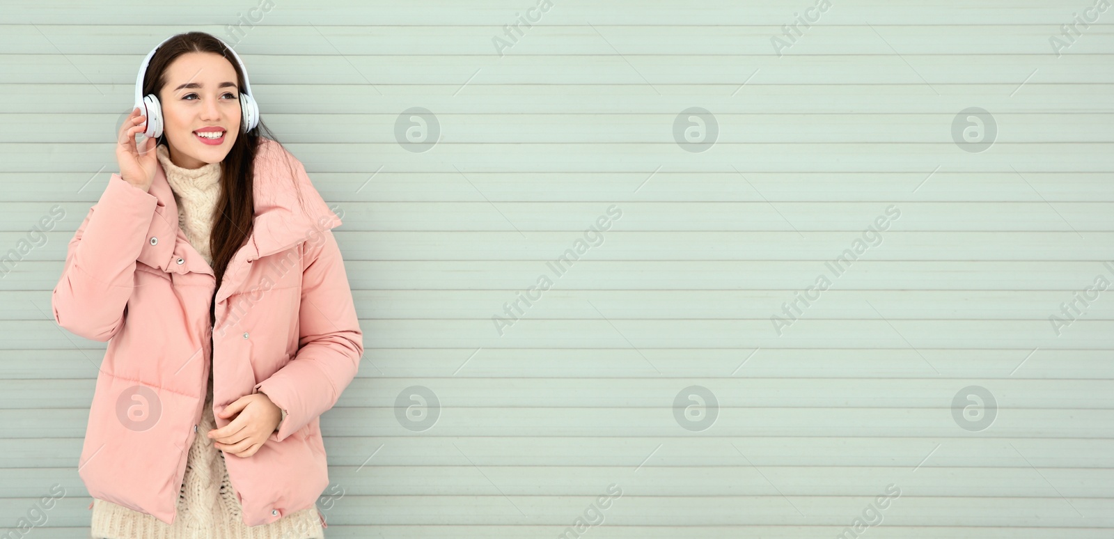 Image of Young woman listening to music with headphones near light wall, space for text. Banner design